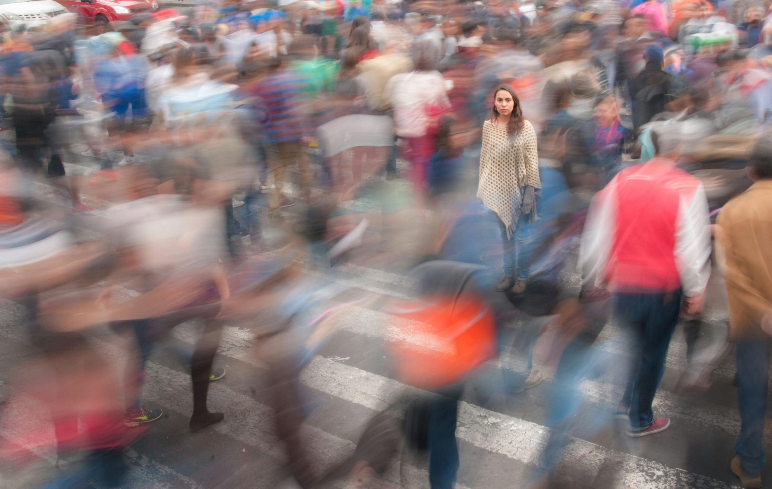 a wonamn standing unmoved in a blurred and rapidly moving crowd